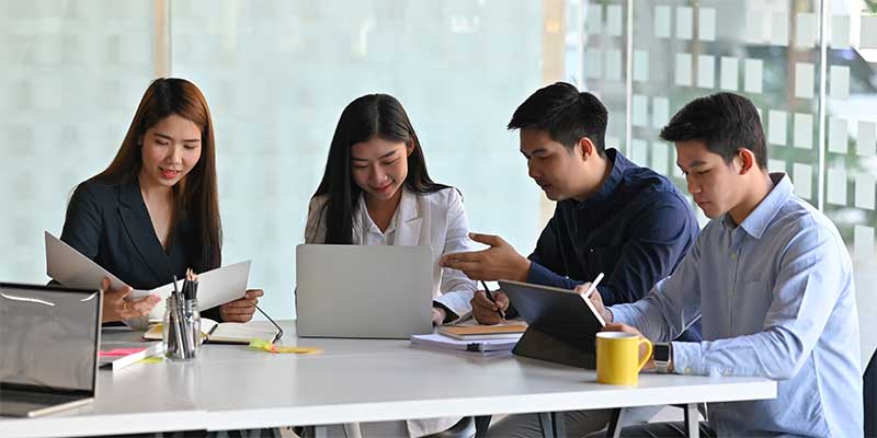 Coworkers talk at a white office desk